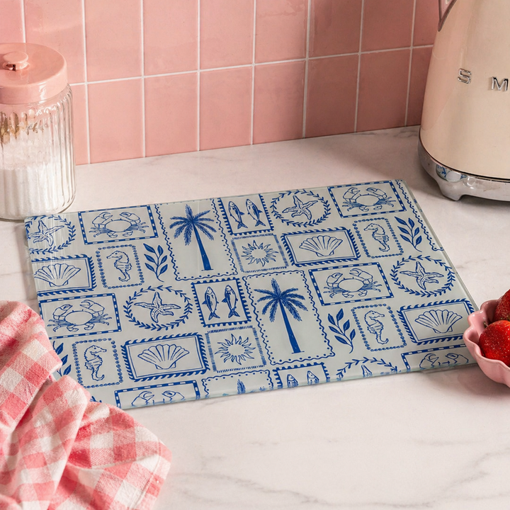 Blue patterned glass cutting board on a kitchen counter with pink tiled wall and vintage-style toaster.