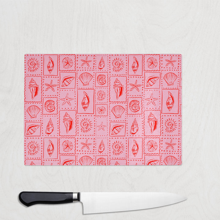 Pink glass chopping board with coral seashells, starfish, and suns in a retro grid – colourful beach kitchen decor