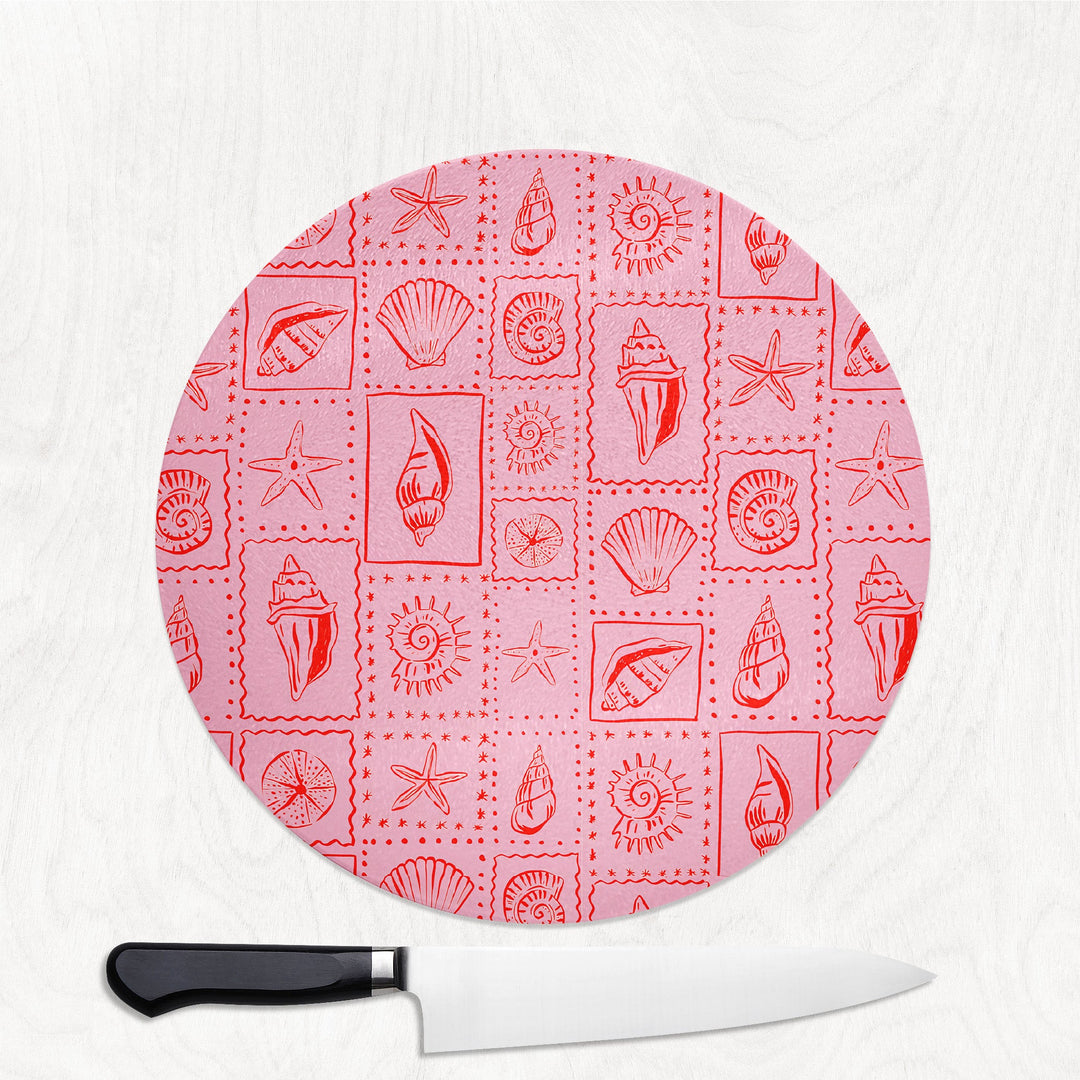 Round pink cutting board with shell pattern and a knife on a white background