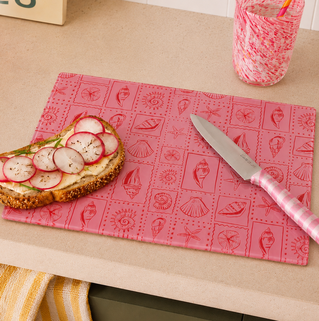 Pink seaside inspired cutting board with bread topped with radishes and a knife on a kitchen counter.