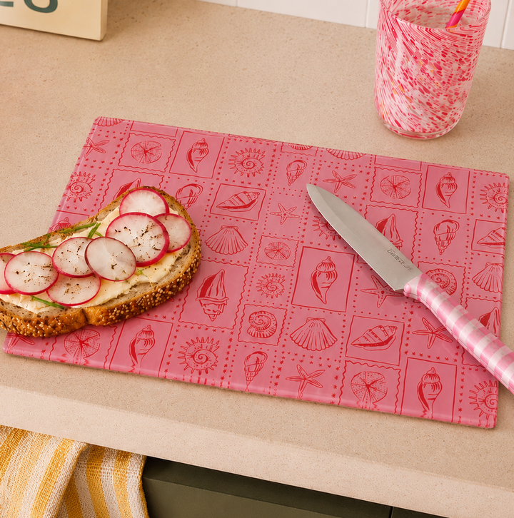Pink seaside inspired cutting board with bread topped with radishes and a knife on a kitchen counter.