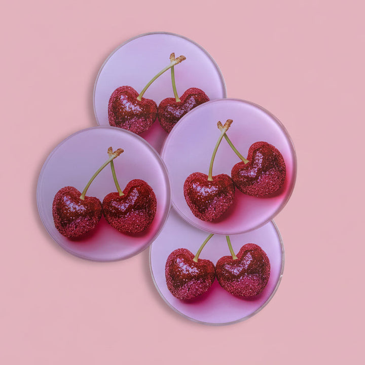 Four pink coasters with cherry design on a wooden surface
