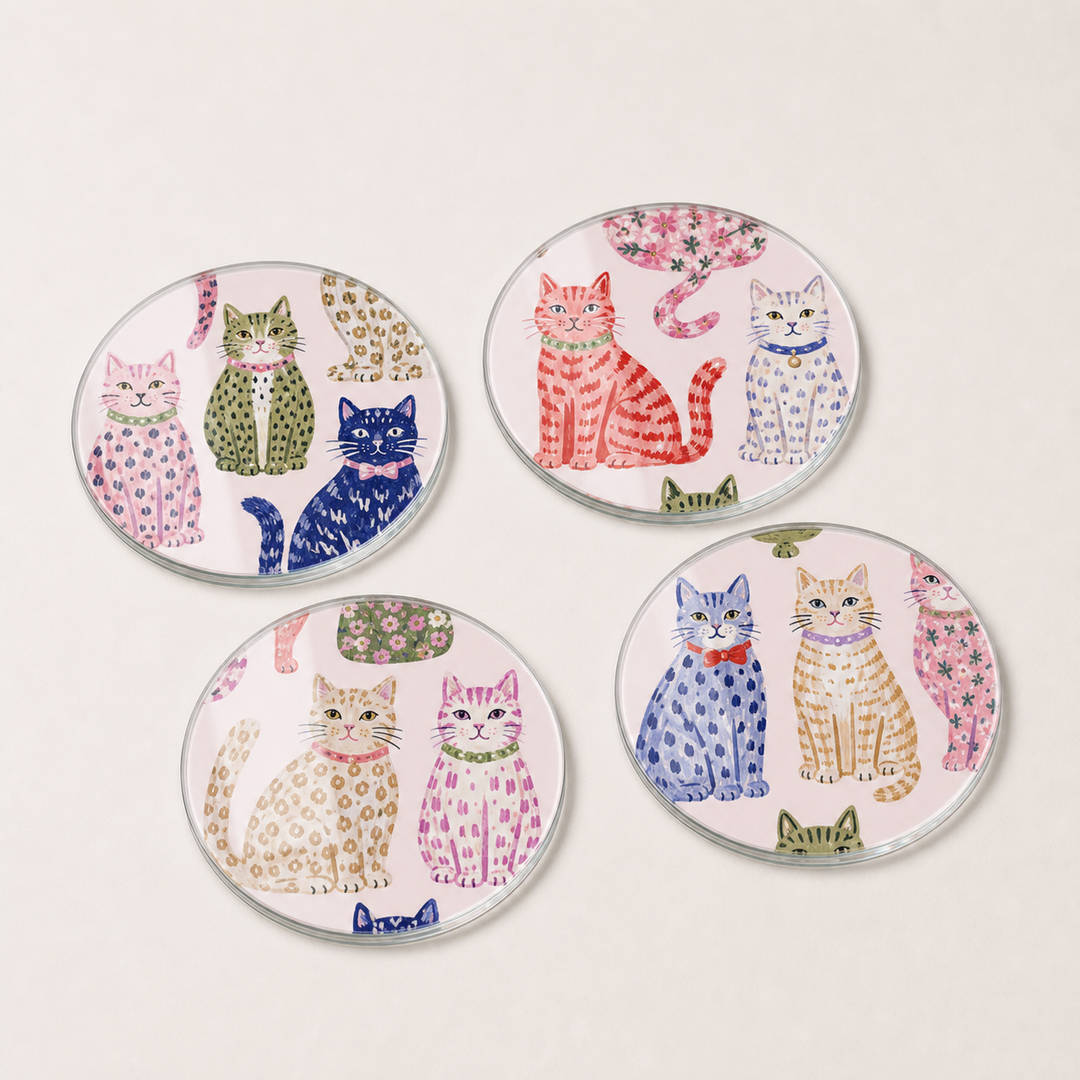 Set of four round glass coasters with colorful cat illustrations on a light pink background.