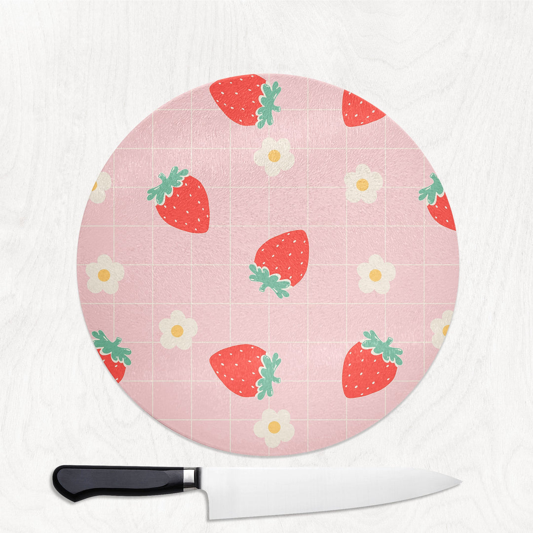 Round pink cutting board with strawberry pattern and a knife on a white background