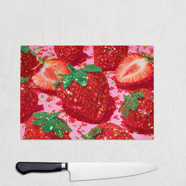 Glass chopping board featuring oversized glitter-style strawberries on a bright pink background
