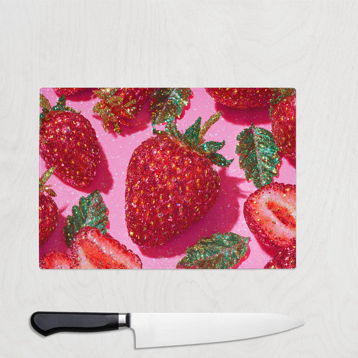 Glass chopping board with oversized glitter-style strawberries on a pink background – bold and colourful kitchen decor