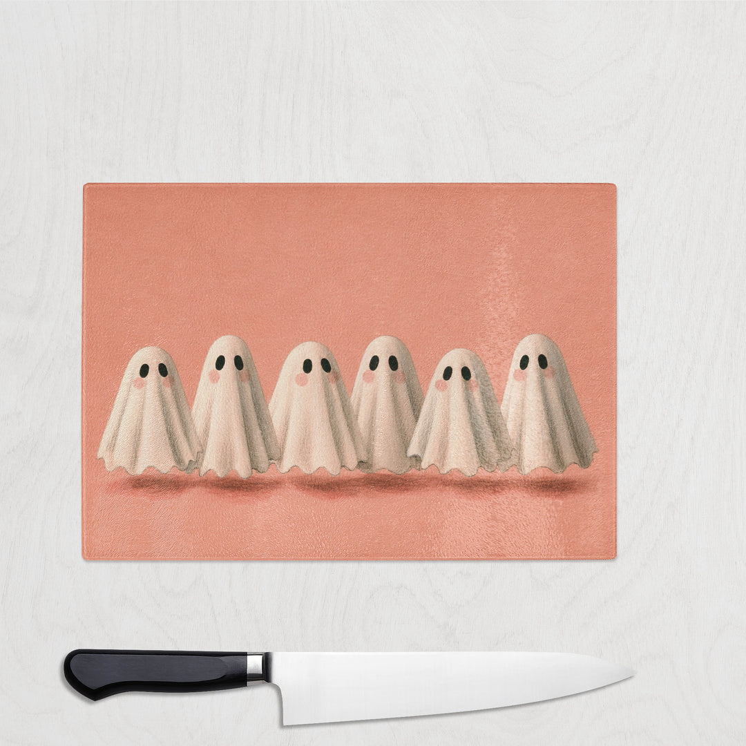 The Cute Ghosts glass chopping board with six little sheet ghosts in a row on warm coral