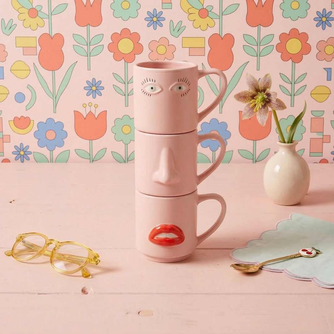 Pink face-shaped mug and jar set against a floral wallpaper background