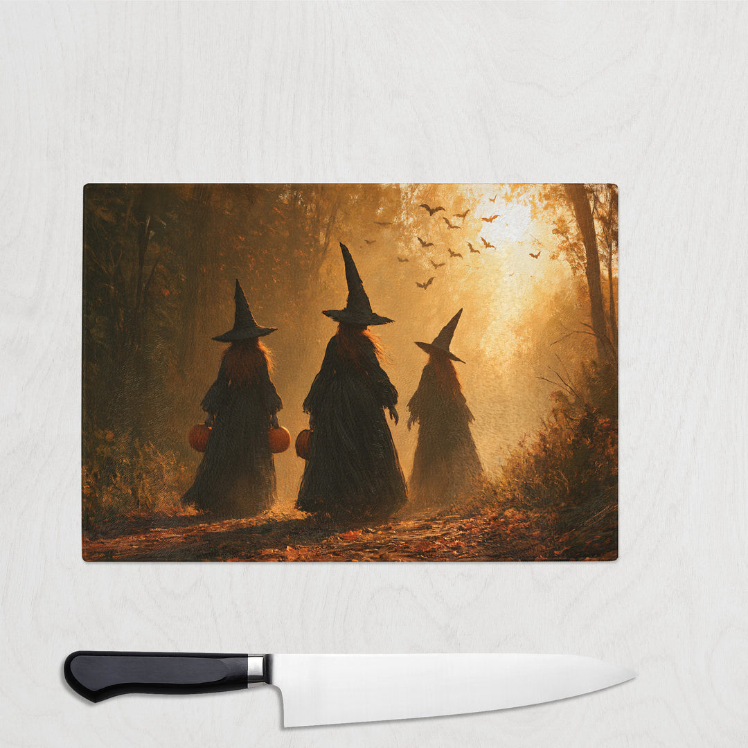 Trick Or Treat Witches glass chopping board with three witches carrying pumpkin buckets through a golden autumn wood