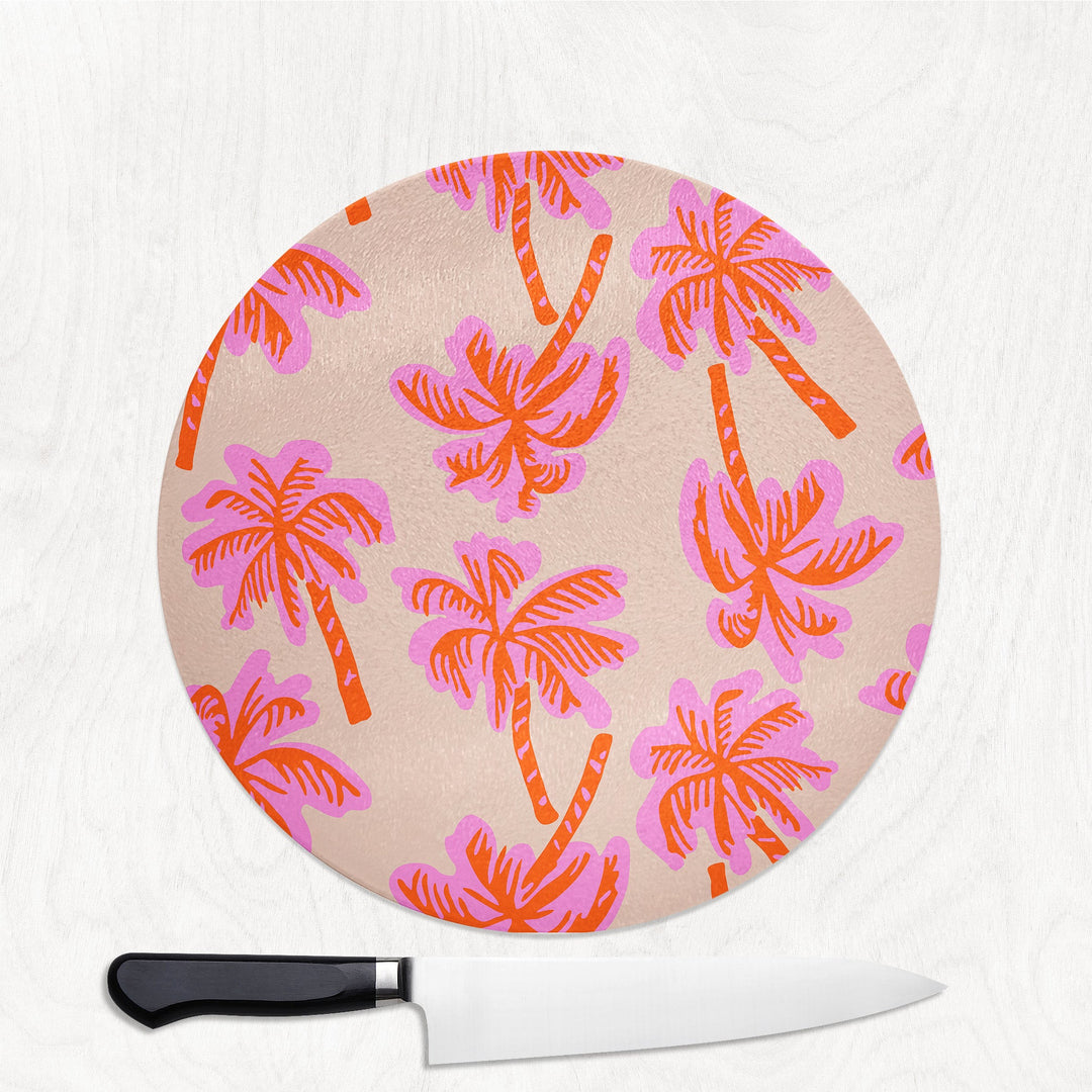 Round cutting board with pink and orange palm tree pattern on a white background