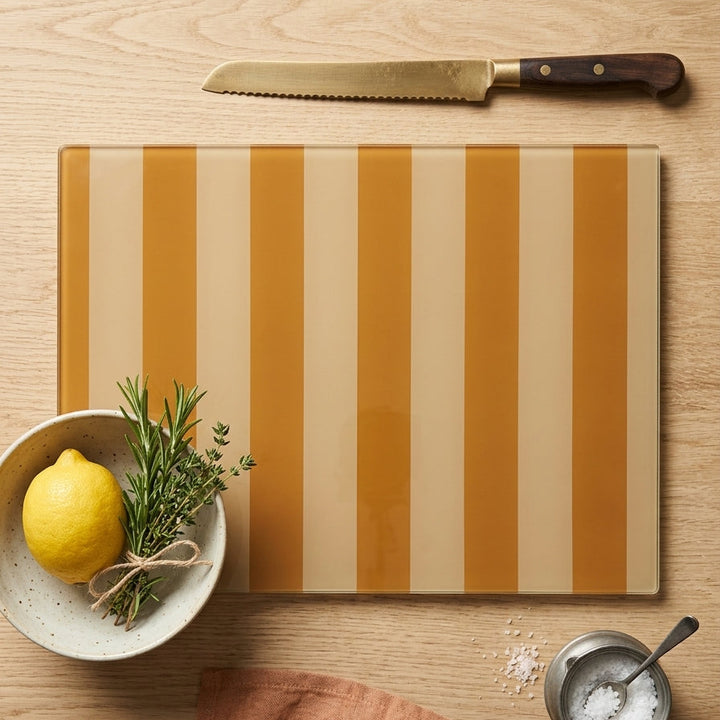 Striped glass cutting board with a lemon, knife, and small bowl on a wooden surface