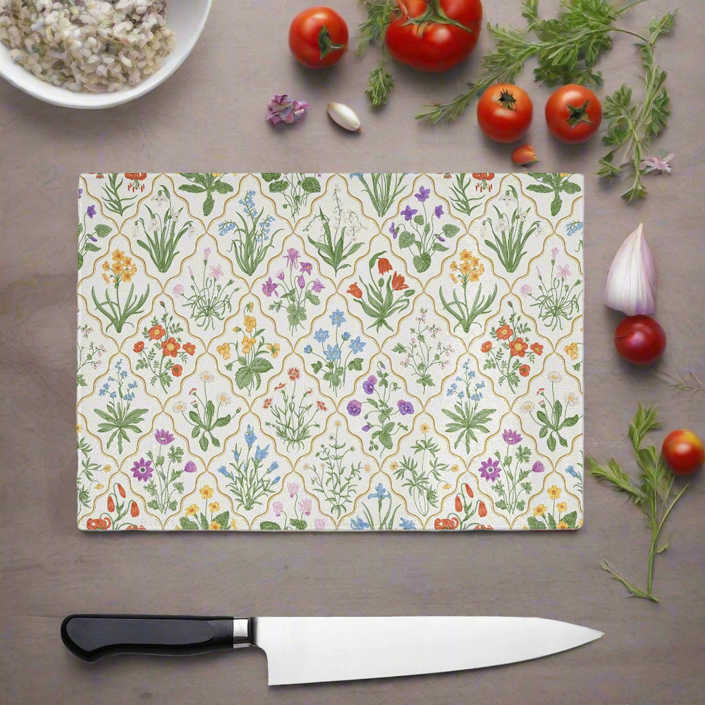 The Yililo Wildflower Harmony Glass Chopping Board brings rustic charm to your kitchen décor, featuring colorful flowers and shown on a table alongside a chef’s knife, tomatoes, fresh herbs, garlic, and a bowl of rice.