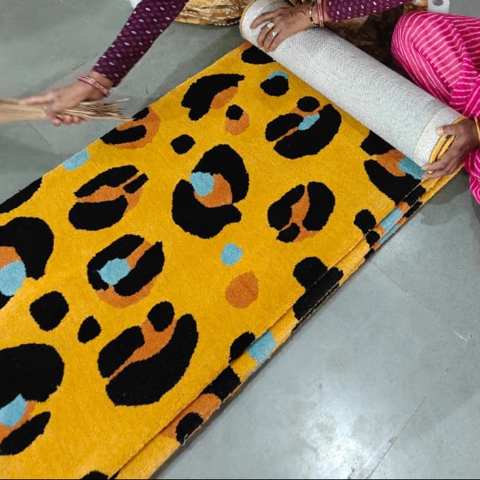 Two women rolling out a leopard print carpet on a store floor with luggage in the background.