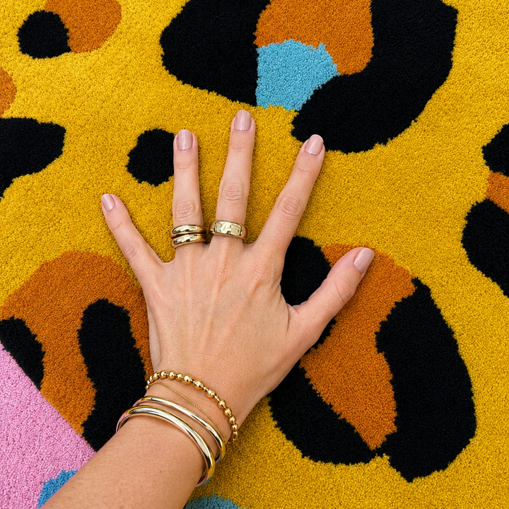Hand with gold rings and bracelets on a multicolored patterned surface