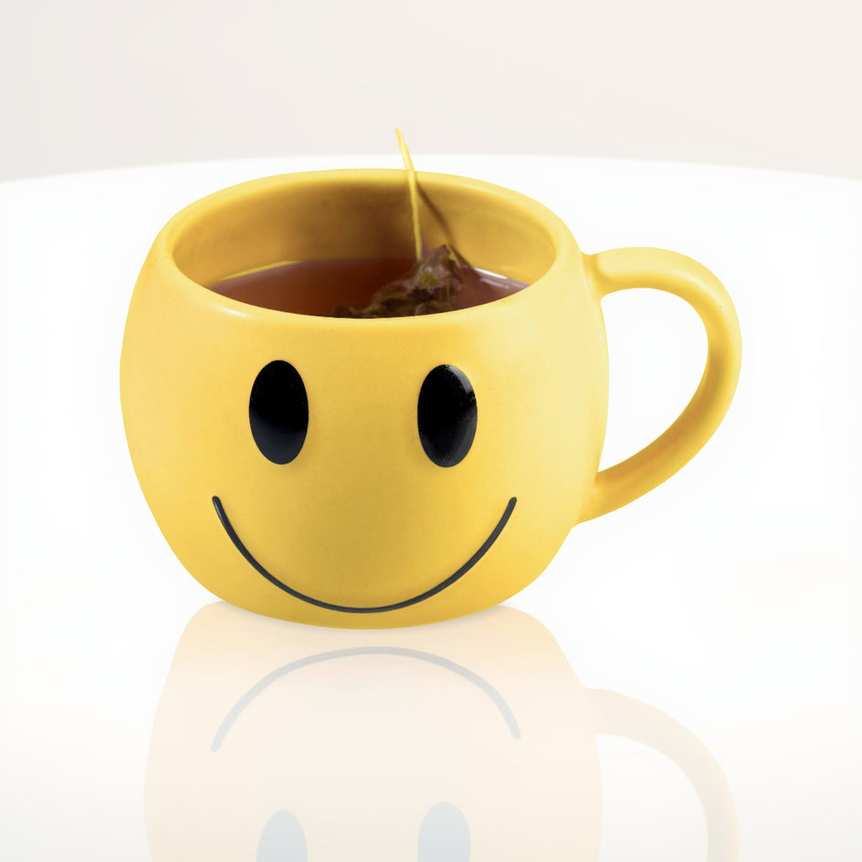 Yellow smiley face mug with tea inside on a white background