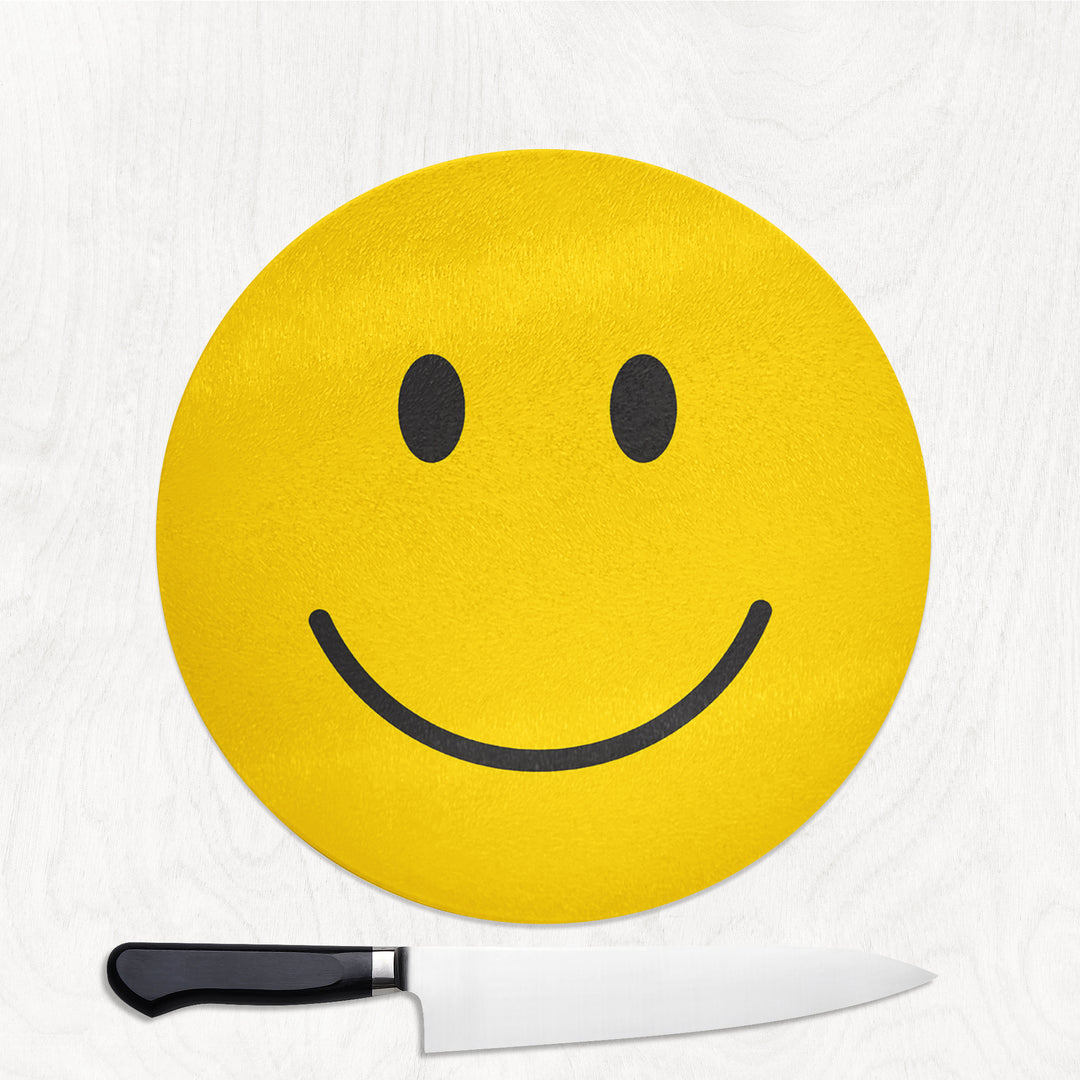 Round yellow smiley face glass chopping board with a knife on a white background