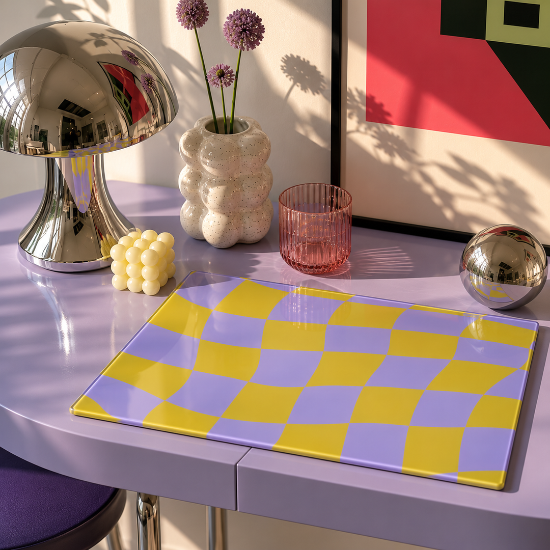 Decorative table setting with a checkered glass chopping board, lamp, vase, and abstract painting.