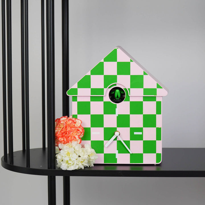 Checkered clock with pink and green pattern on a black surface with flowers