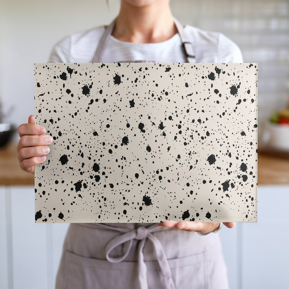 Glass chopping board with black ink splatter pattern on a cream background