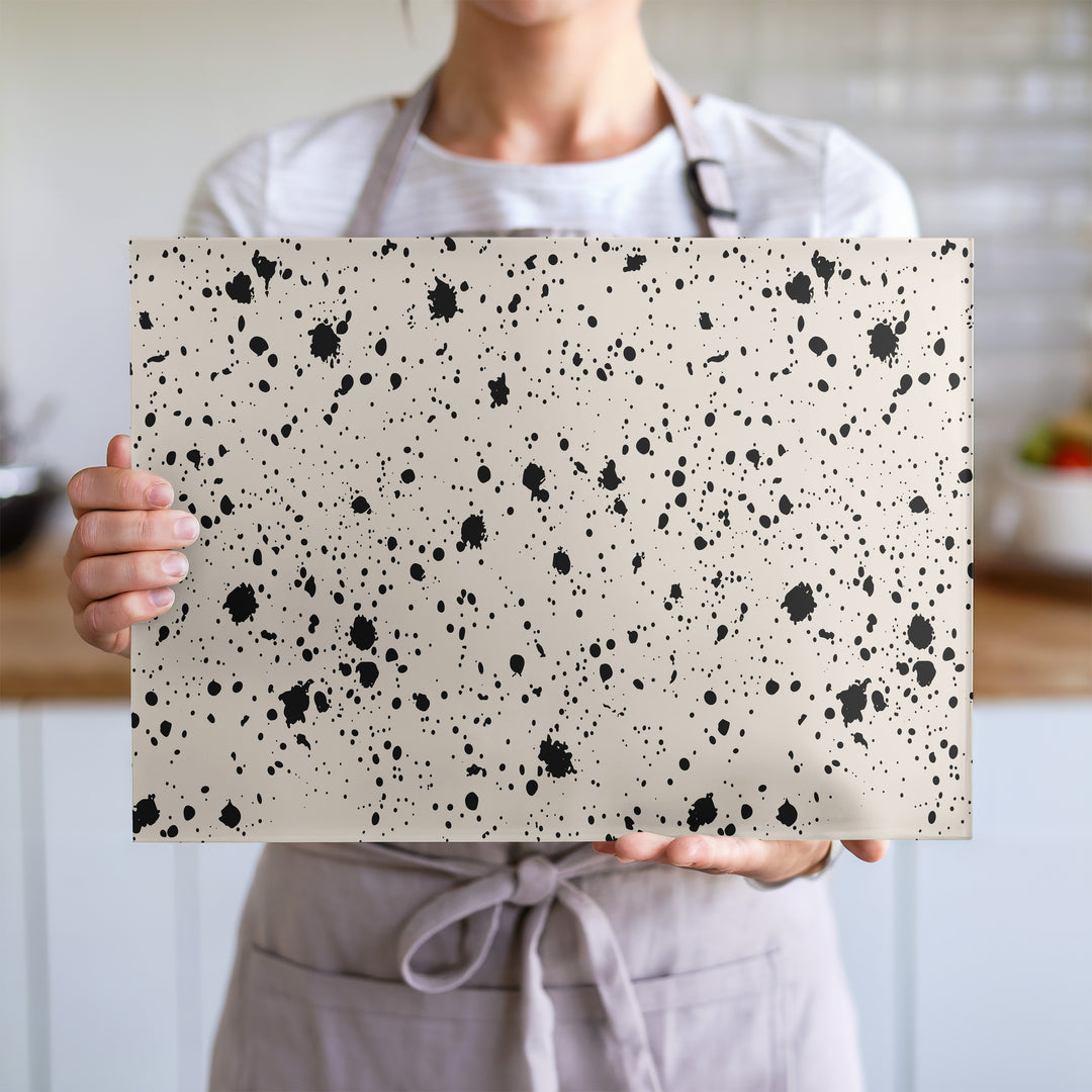 Glass chopping board with black ink splatter pattern on a cream background
