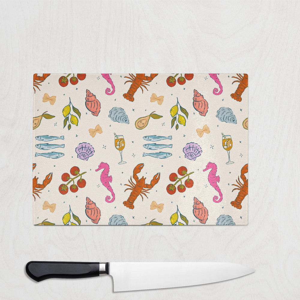 Colourful repeat print of lobsters, lemons, Aperol spritz glasses, seahorses and pasta on a glass chopping board – summery and fun kitchen accessory.