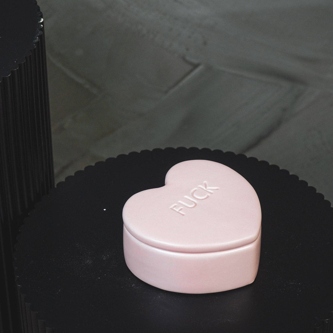 Pink heart-shaped box with 'FUCK' on a black surface