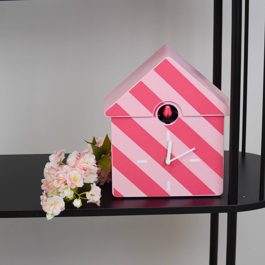 Pink striped cuckoo clock on a black shelf with flowers