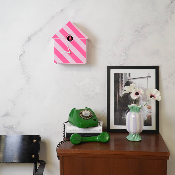 Decorative items including a pink and white striped clock, green phone, and framed picture on a wooden surface.