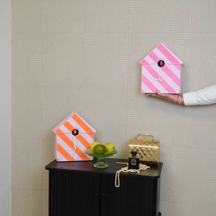 Pink and orange striped birdhouse on a gray wall with a hand holding it.