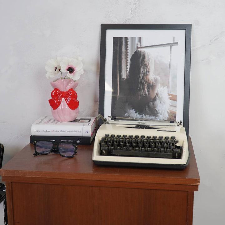 Vintage typewriter on a wooden desk with a framed photo and decorative items.