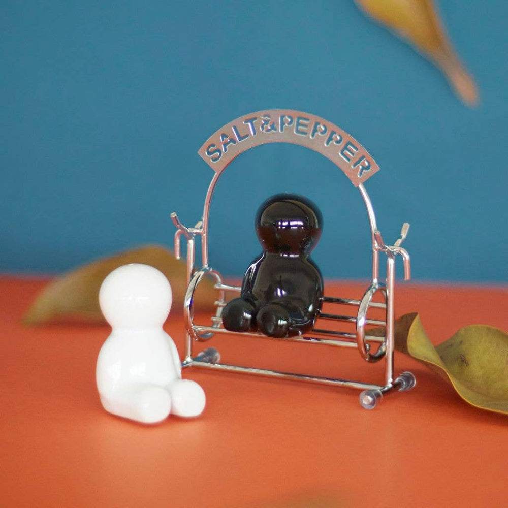 Salt and pepper shakers with a decorative holder on an orange surface with a blue background