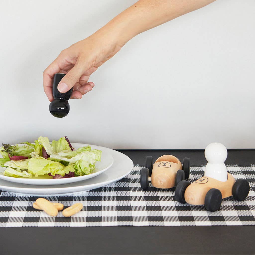 Wooden race car salt and pepper shakers on a checkered tablecloth with a salad plate.