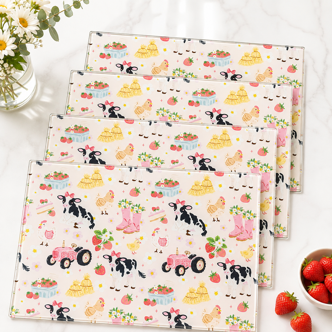 Stack of Yililo Cute Farmyard Life glass placemats, printed with cows, chickens, tractors and strawberries.