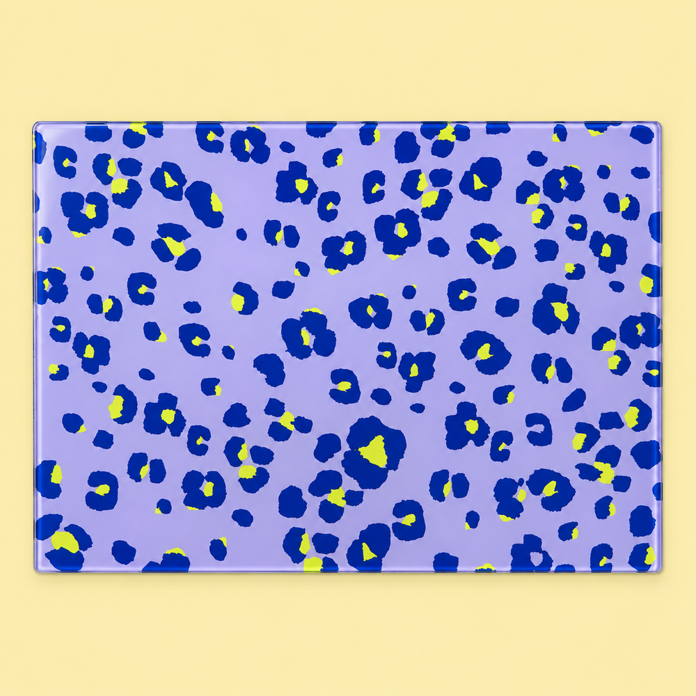 Lilac Lime Neon Leopard glass chopping board with navy and lime leopard spots on lilac, laid flat on a pale yellow background