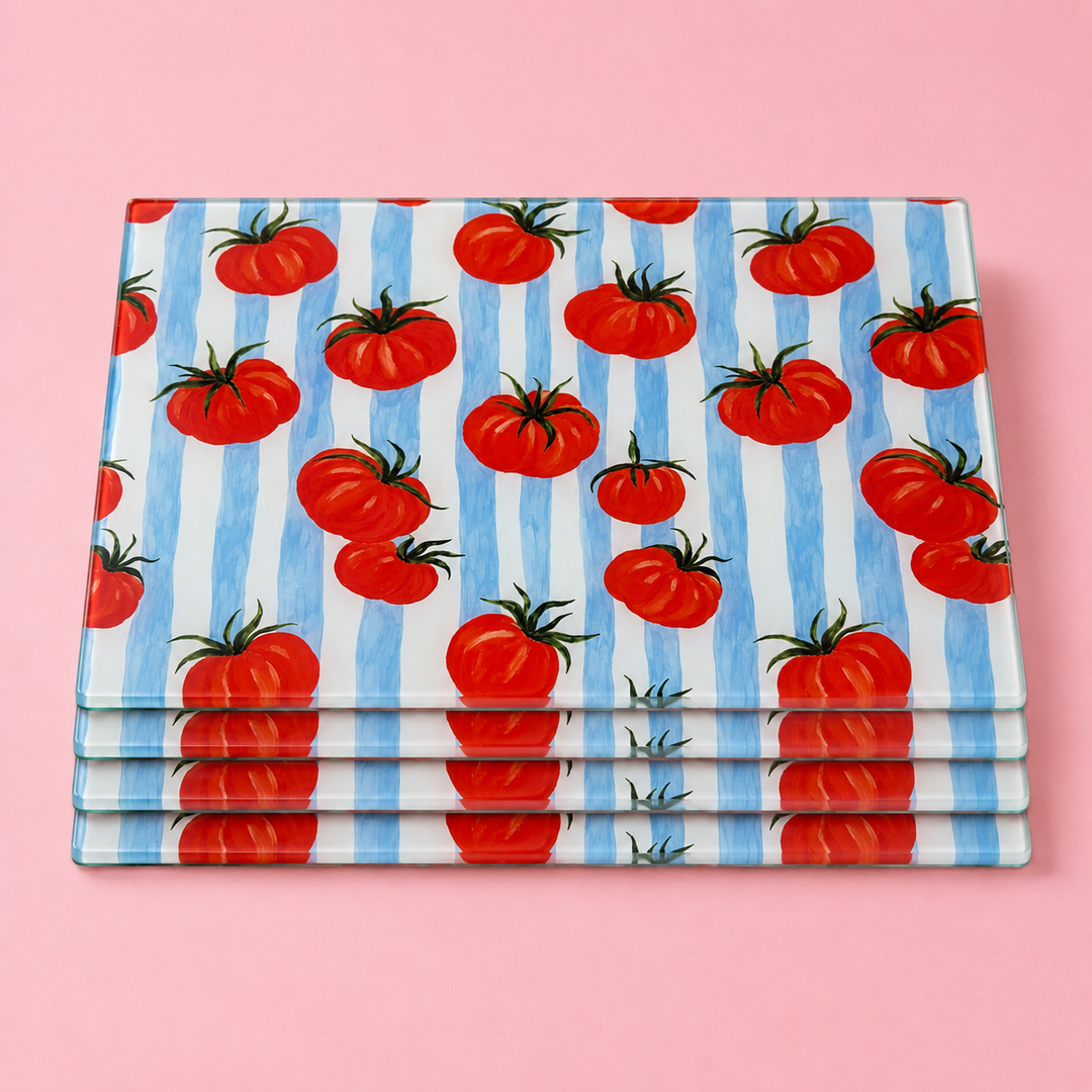 Stack of Yililo Tomato and Stripes glass placemats, red tomatoes on blue and cream stripes, on a pink background.