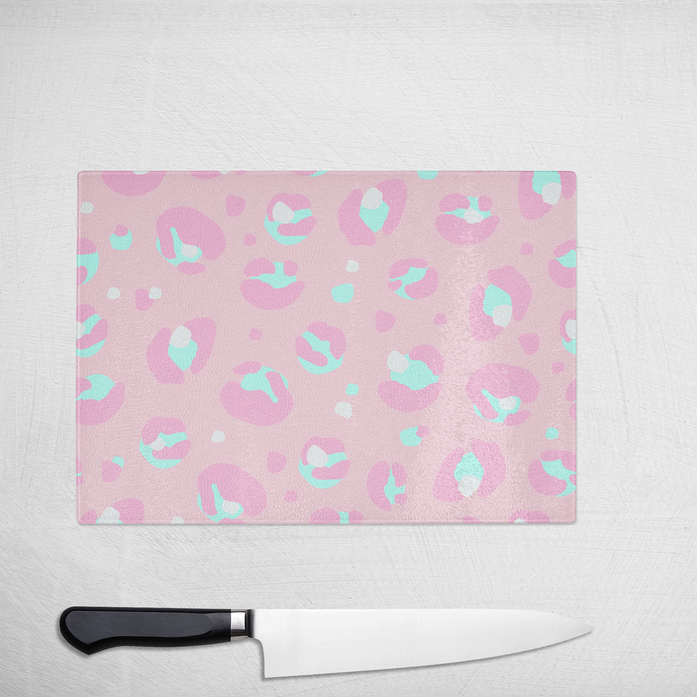 The Yililo Light Pink Leopard Print Glass Chopping Board rests on a white surface beside a black-handled chef’s knife—making it an ideal kitchen gift for any home cook.